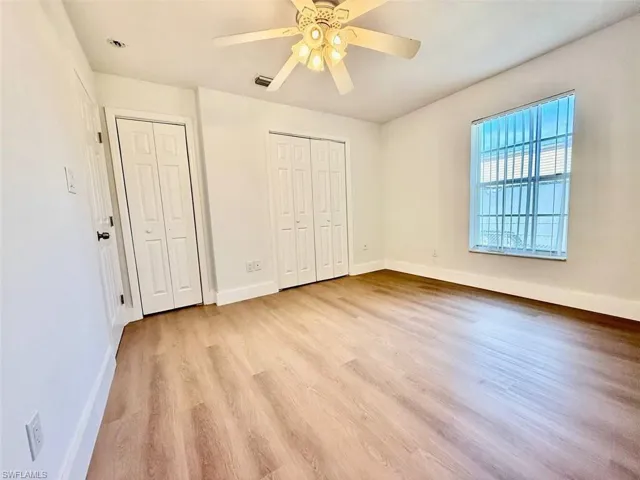 Unfurnished bedroom with light wood-type flooring, ceiling fan, and two closets