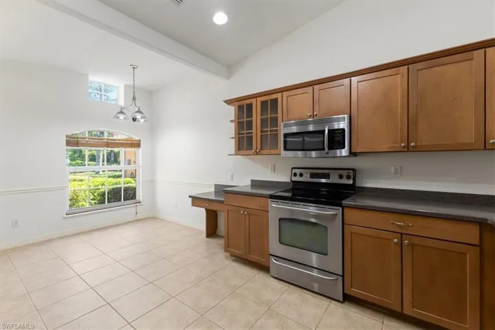 Kitchen featuring vaulted ceiling with beams, an inviting chandelier, appliances with stainless steel finishes, and a wealth of natural light
