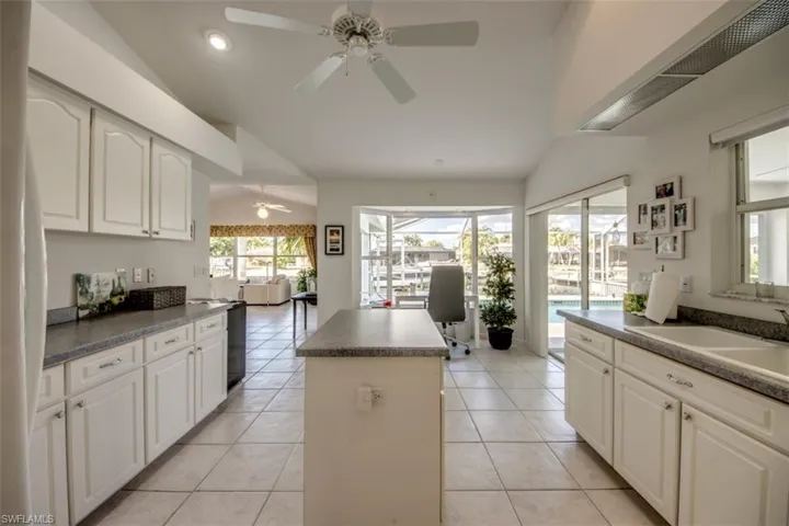 Kitchen with vaulted ceiling, white cabinetry, dark countertops, a center island, and ceiling fan
