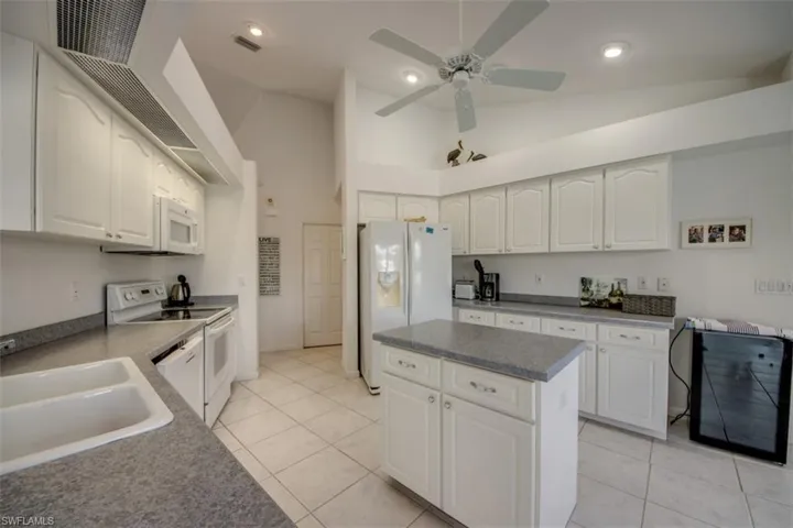 Kitchen with white cabinetry, white appliances, vaulted ceiling, a kitchen island, and recessed lighting