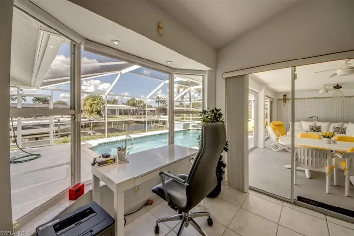 Home office with a sunroom, a water view, vaulted ceiling, ceiling fan, and light tile patterned floors
