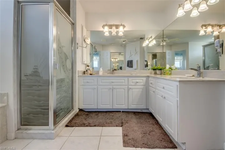 Full bathroom with double vanity, ceiling fan, a marble finish shower, and light tile patterned floors