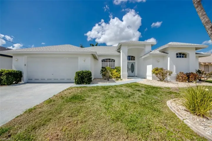 View of front facade with a garage, stucco siding, driveway, and a front lawn