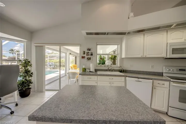 Kitchen featuring white appliances, dark countertops, light tile patterned floors, white cabinetry, and plenty of natural light
