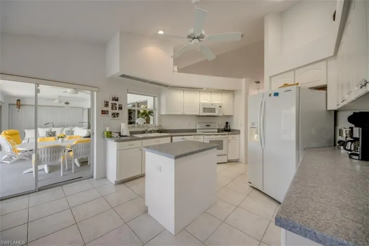 Kitchen featuring ceiling fan, white cabinets, white appliances, a kitchen island, and vaulted ceiling