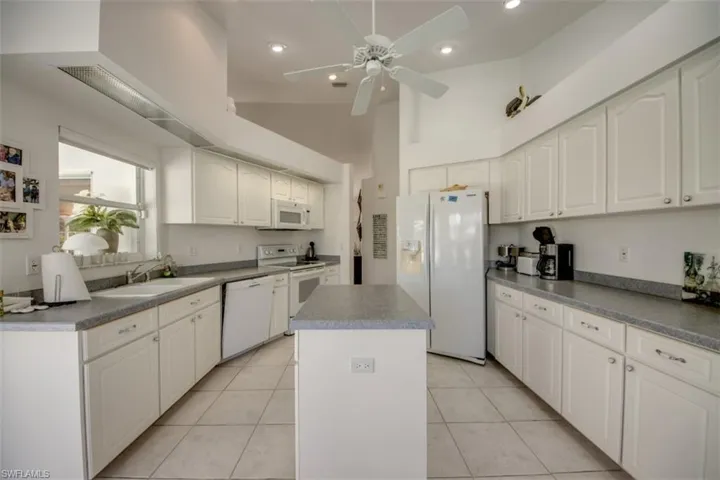 Kitchen featuring white appliances, a high ceiling, a center island, white cabinetry, and ceiling fan