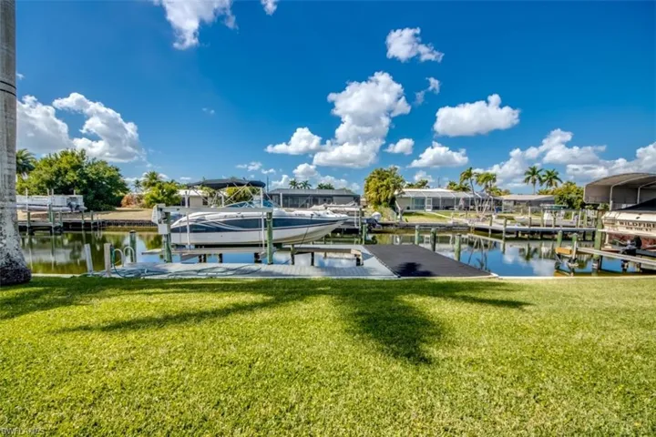 Dock area featuring boat lift, a lawn, and a water view