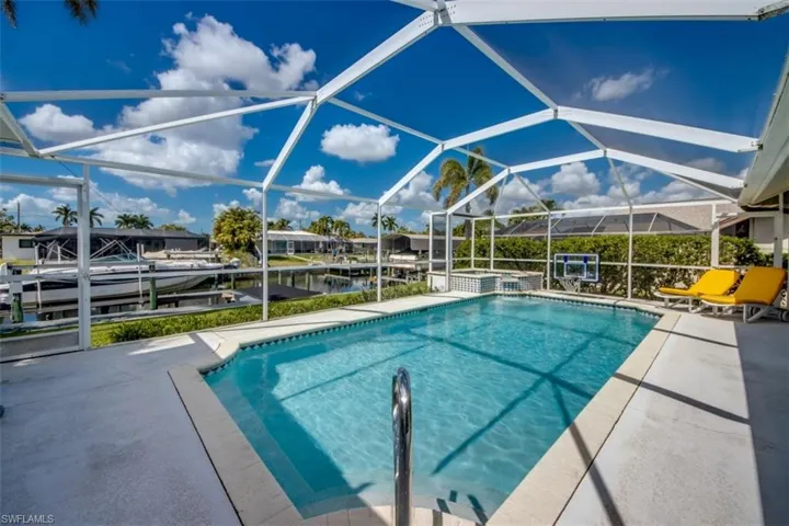 Relaxing pool / spa with a sunroom, a patio area, glass enclosure, a boat dock, and a water view