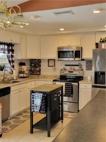 Kitchen featuring white cabinets, stove, refrigerator, sink, and light tile floors