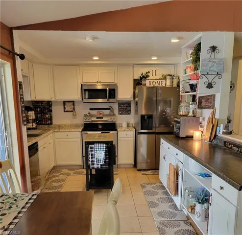Kitchen featuring white cabinets, lofted ceiling, light tile floors, and appliances with stainless steel finishes