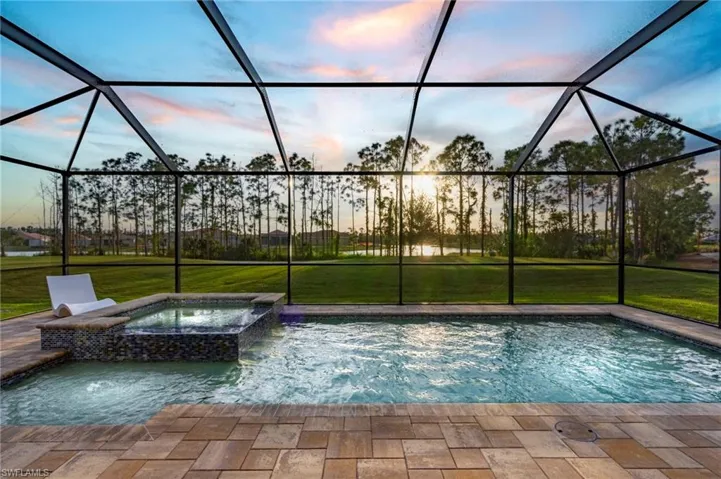 Pool at dusk featuring glass enclosure, an in ground hot tub, pool water feature, and a lawn