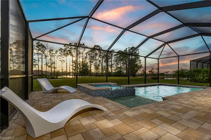 Pool at dusk featuring a patio area, an in ground hot tub, and a lanai
