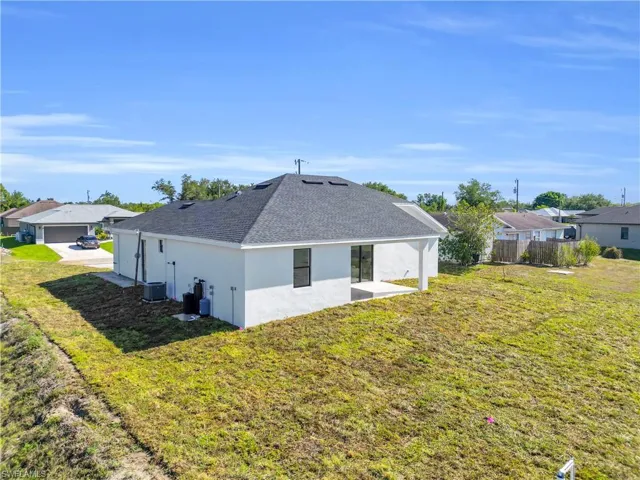 Rear view of property with roof with shingles, stucco siding, central AC, a yard, and fence