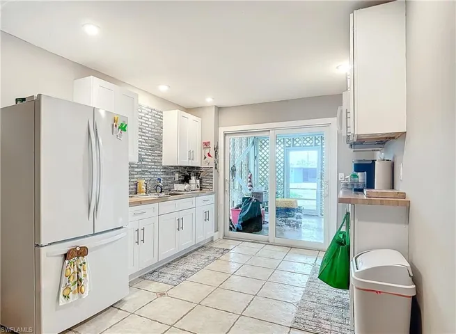 Kitchen with white cabinetry, white fridge, tasteful backsplash, and light tile flooring
