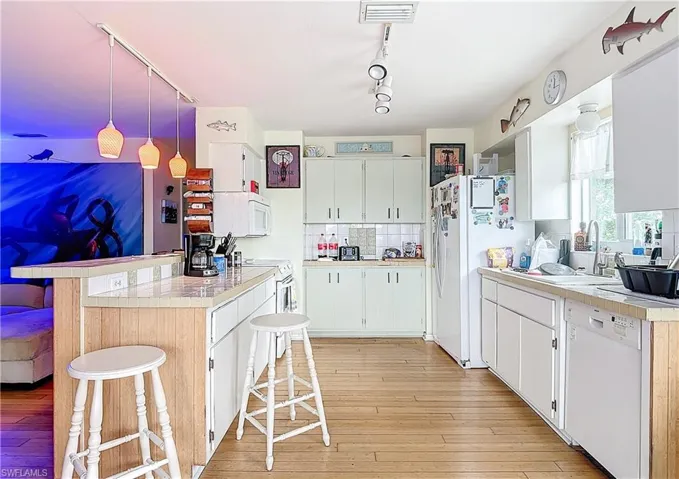 Kitchen with a kitchen breakfast bar, white cabinetry, white appliances, and rail lighting