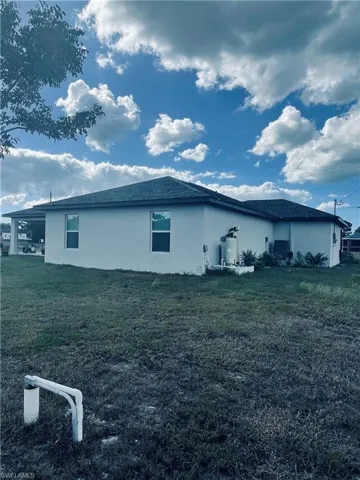 View of side of property with stucco siding, a lawn, and roof with shingles