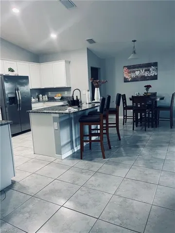 Kitchen with refrigerator with ice dispenser, dark stone countertops, a breakfast bar area, a peninsula, and pendant lighting