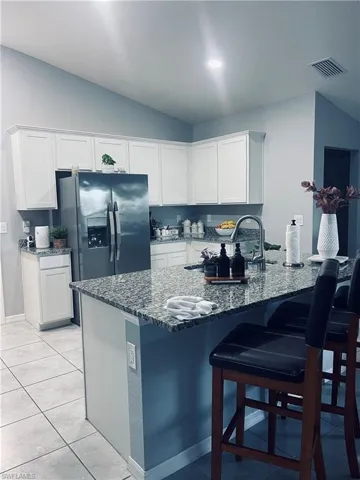 Kitchen featuring white cabinetry, dark stone counters, stainless steel fridge, a kitchen bar, and light tile patterned floors