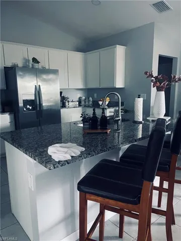 Kitchen featuring dark stone countertops, a breakfast bar area, stainless steel fridge, light tile patterned floors, and vaulted ceiling