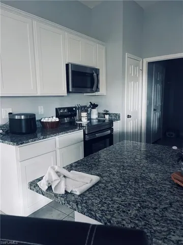 Kitchen with white cabinetry, electric range oven, dark stone countertops, and tile patterned flooring