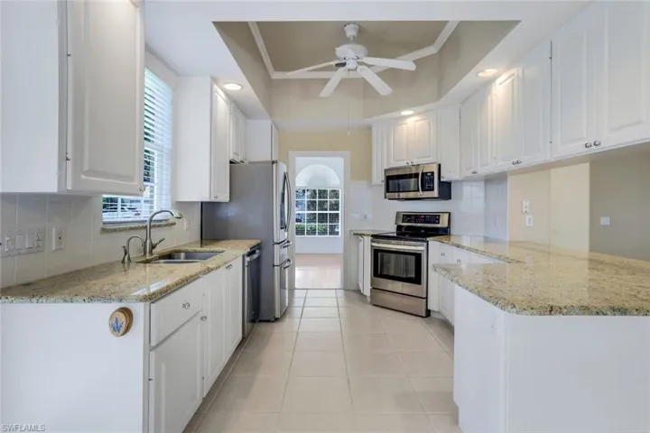Kitchen featuring crown molding, appliances with stainless steel finishes, white cabinets, sink, and ceiling fan