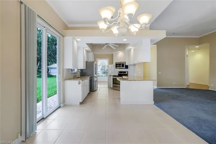 Kitchen with kitchen peninsula, stainless steel appliances, light stone counters, light colored carpet, and white cabinets
