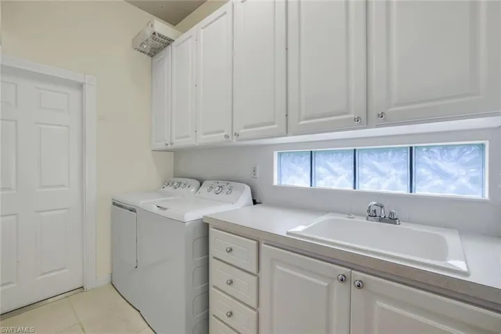 Clothes washing area with cabinets, sink, light tile flooring, and washing machine and clothes dryer