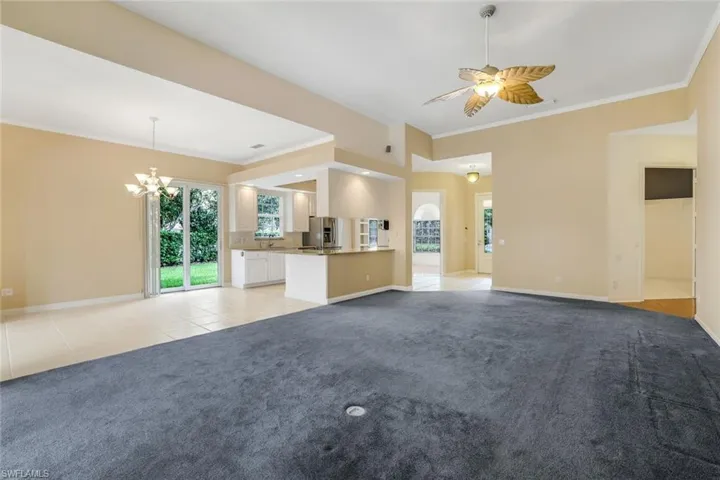 Unfurnished living room featuring a healthy amount of sunlight, ornamental molding, light colored carpet, and ceiling fan with notable chandelier