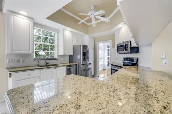 Kitchen featuring sink, white cabinets, light stone countertops, and stainless steel appliances