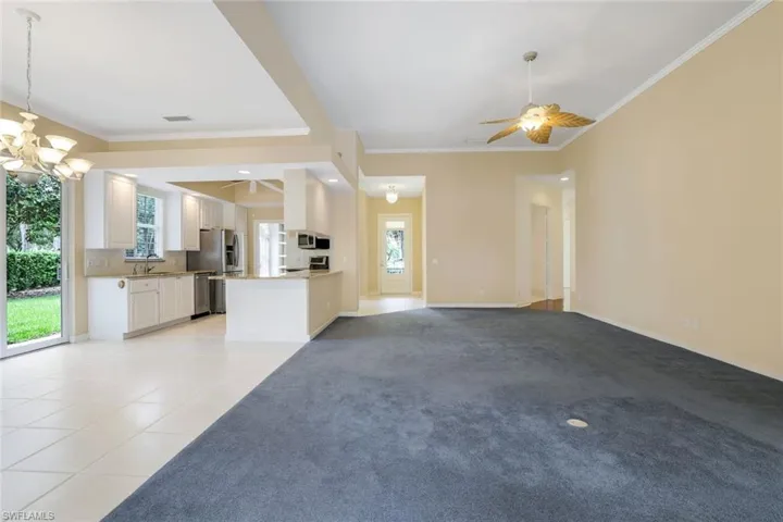 Unfurnished living room with sink, ornamental molding, light tile floors, and ceiling fan with notable chandelier