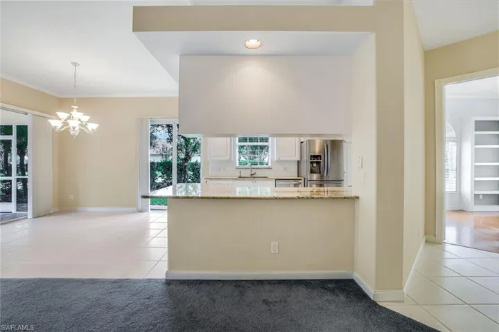 Kitchen featuring light stone counters, light tile flooring, hanging light fixtures, stainless steel fridge, and white cabinets