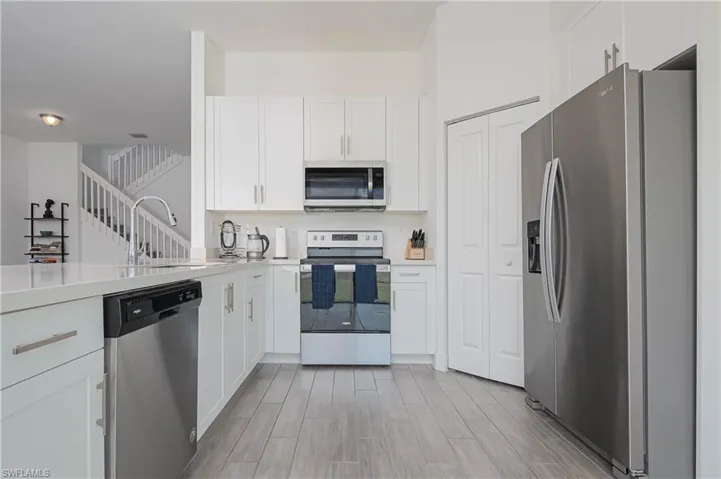 Kitchen featuring appliances with stainless steel finishes, white cabinetry, wood finish floors, and light stone countertops