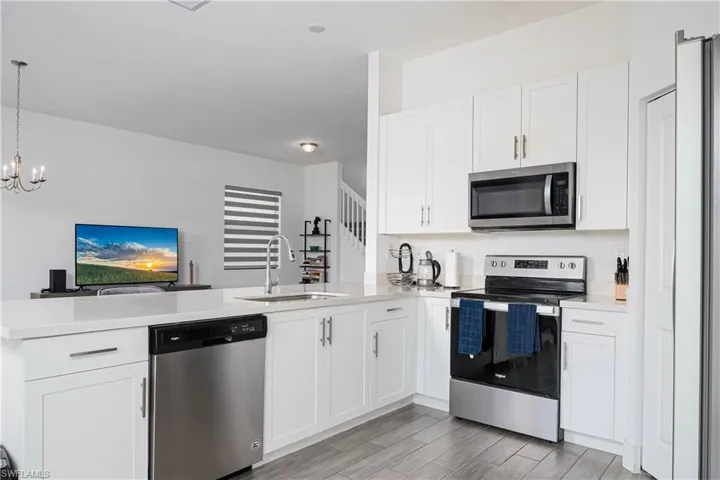 Kitchen featuring appliances with stainless steel finishes, white cabinets, a peninsula, wood finish floors, and decorative light fixtures