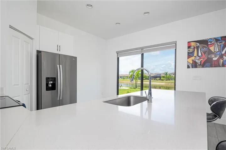 Kitchen with stainless steel refrigerator with ice dispenser, light stone countertops, white cabinetry, recessed lighting, and a water view