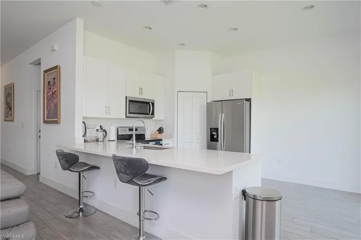 Kitchen featuring appliances with stainless steel finishes, a peninsula, white cabinetry, wood finish floors, and a breakfast bar area