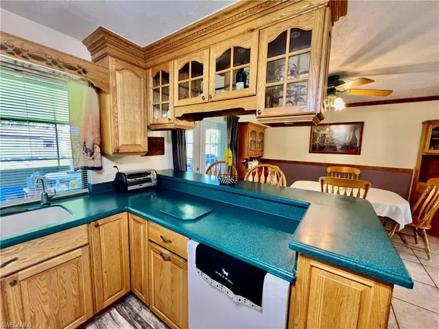 Kitchen with white dishwasher, light tile patterned flooring, a sink, solid surface countertops, and glass insert cabinets