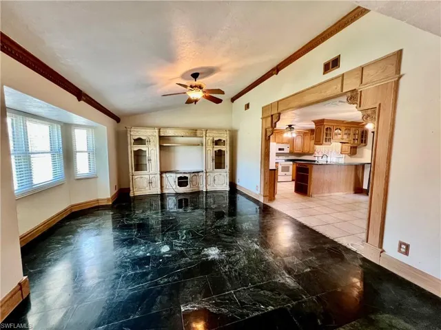 Living room with marble floors, a ceiling fan, ornamental molding, and cathedral ceilings.