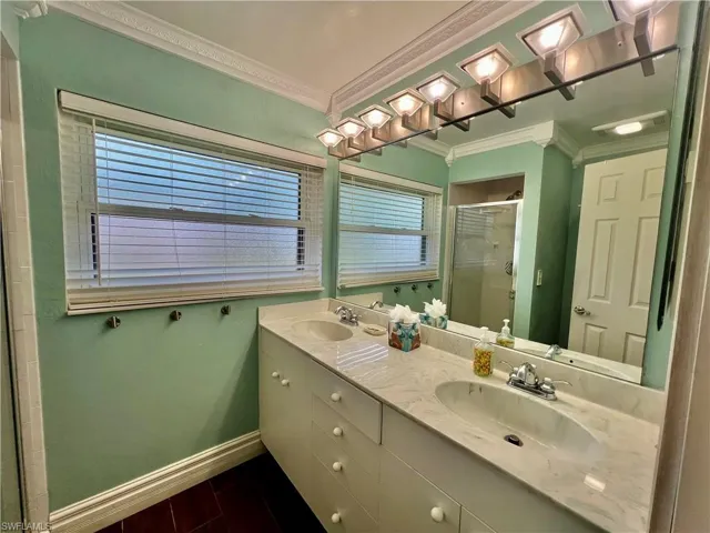 Primary bathroom with dual sinks, ornamental molding, and a stall shower