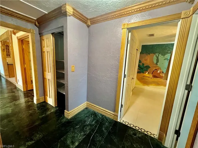 Hall with a textured wall, baseboards, a textured ceiling, and crown molding