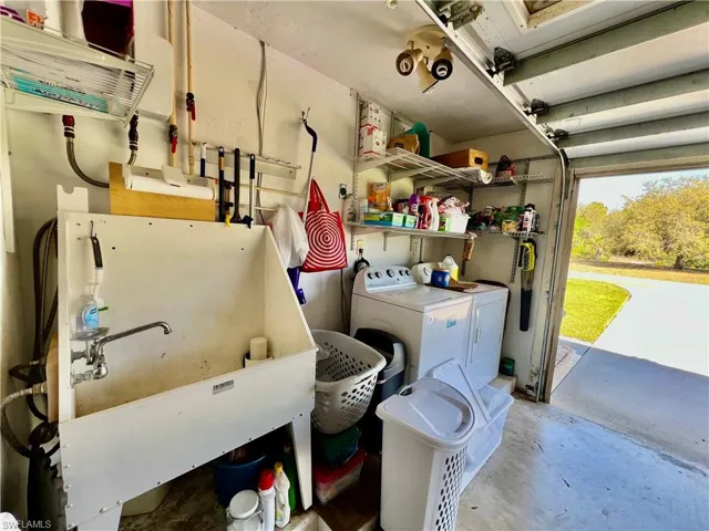 Garage featuring washer and dryer, laundry tub and tankless water heater.