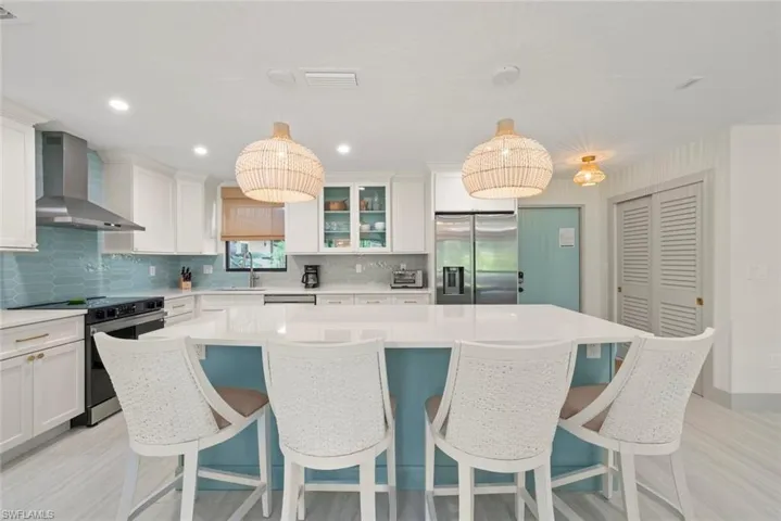 Kitchen featuring appliances with stainless steel finishes, a center island, wall chimney exhaust hood, white cabinets, and tasteful backsplash