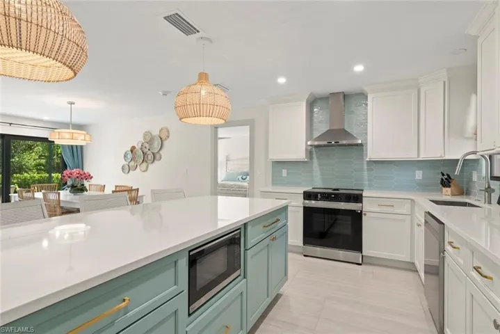 Kitchen featuring appliances with stainless steel finishes, pendant lighting, white cabinets, wall chimney range hood, and recessed lighting