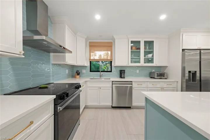 Kitchen featuring stainless steel appliances, wall chimney range hood, white cabinets, light stone countertops, and recessed lighting