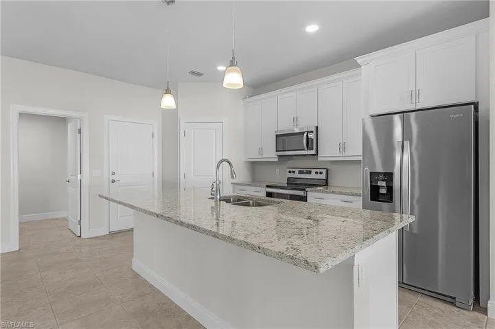 Kitchen featuring appliances with stainless steel finishes, sink, white cabinetry, decorative light fixtures, and an island with sink