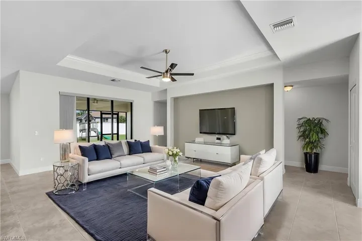 Living room with light tile patterned floors, ceiling fan, and a raised ceiling