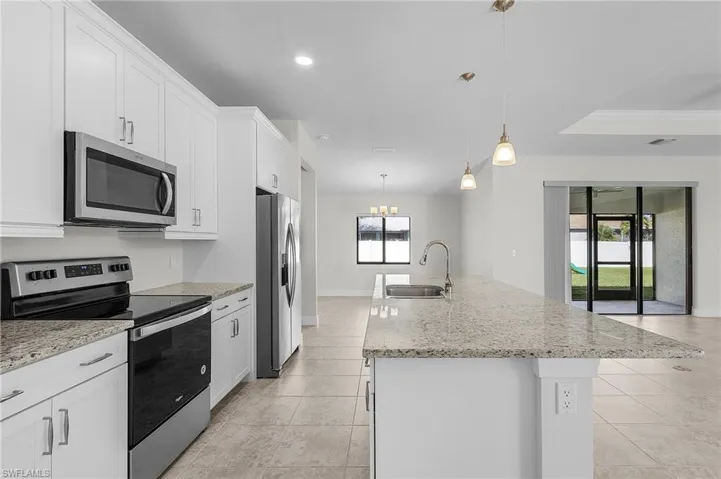 Kitchen with white cabinetry, a kitchen island with sink, stainless steel appliances, and decorative light fixtures
