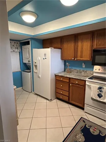 Kitchen with stacked washer / dryer, white fridge with ice dispenser, light tile patterned flooring, and stove