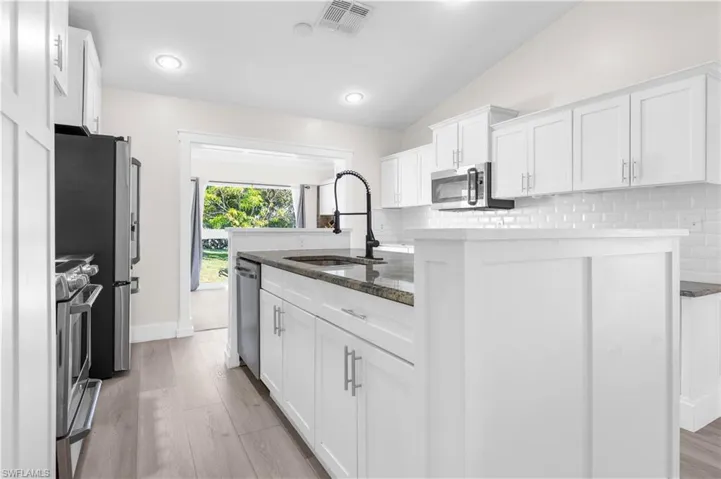 Kitchen featuring white cabinetry, sink, stainless steel appliances, vaulted ceiling, and decorative backsplash