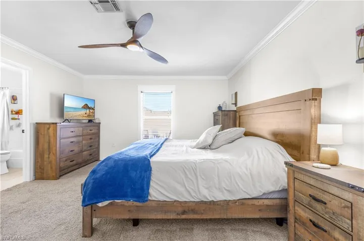 Bedroom with ensuite bathroom, ceiling fan, light colored carpet, and ornamental molding