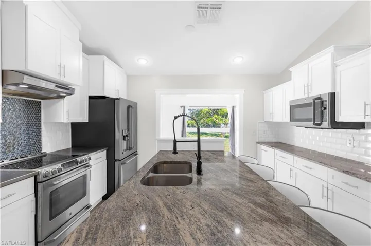 Kitchen featuring appliances with stainless steel finishes, ventilation hood, sink, dark stone countertops, and white cabinetry